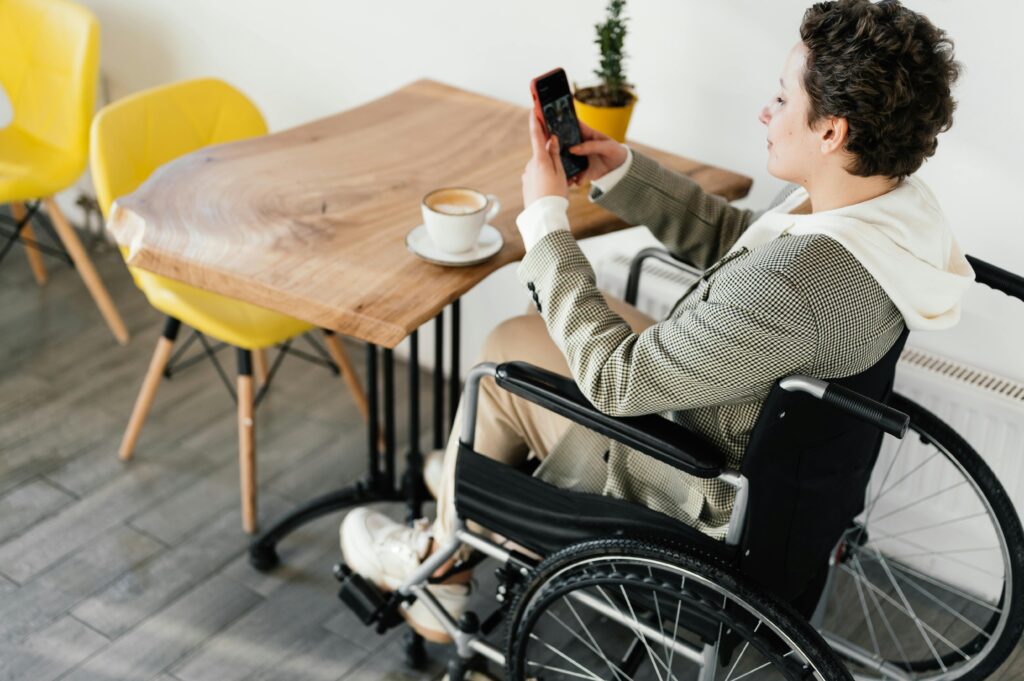 Side view full body of female in wheelchair taking picture of hot coffee while sitting at wooden table in cafeteria